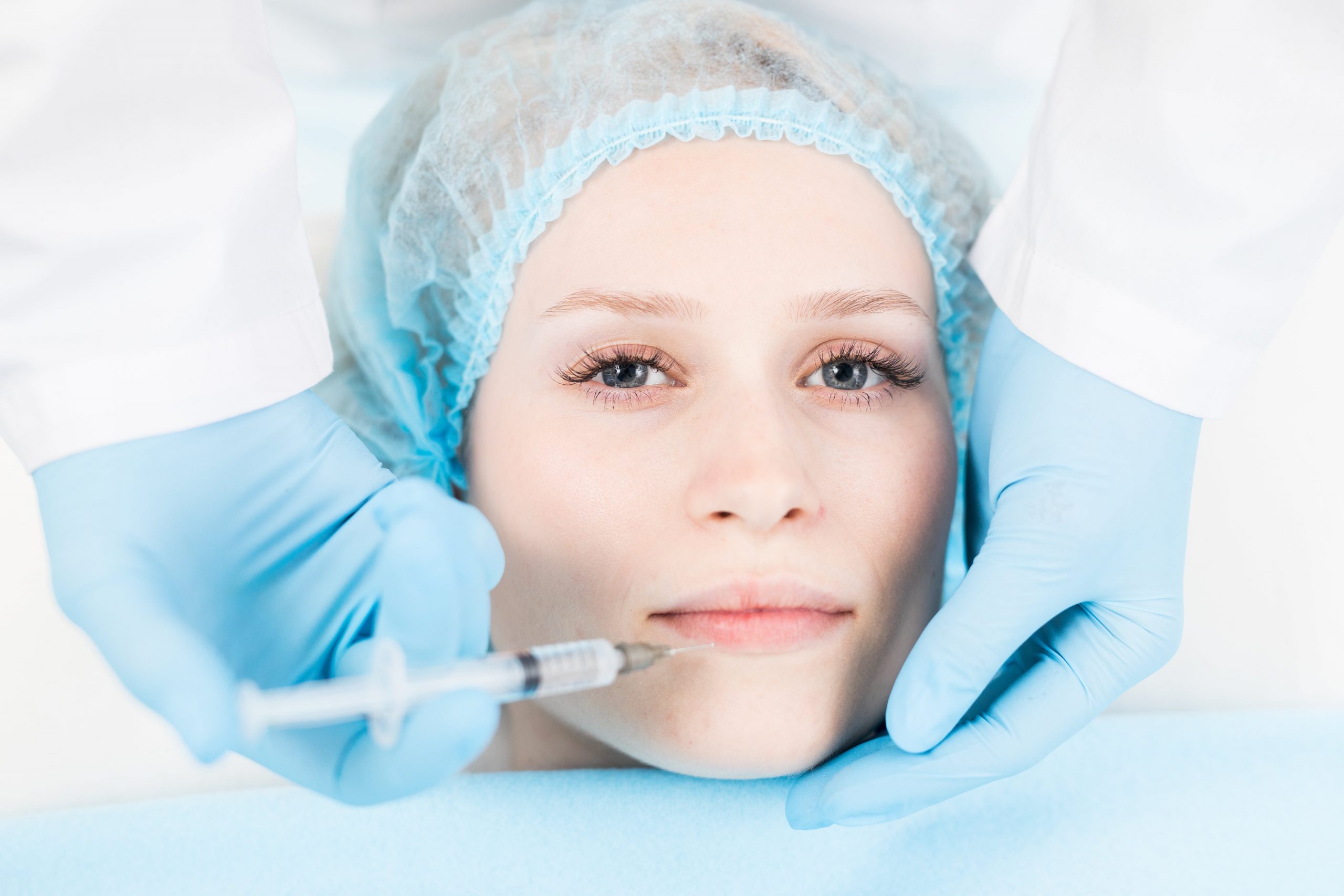 Young woman looking at camera while having lip filler injection in beauty spa